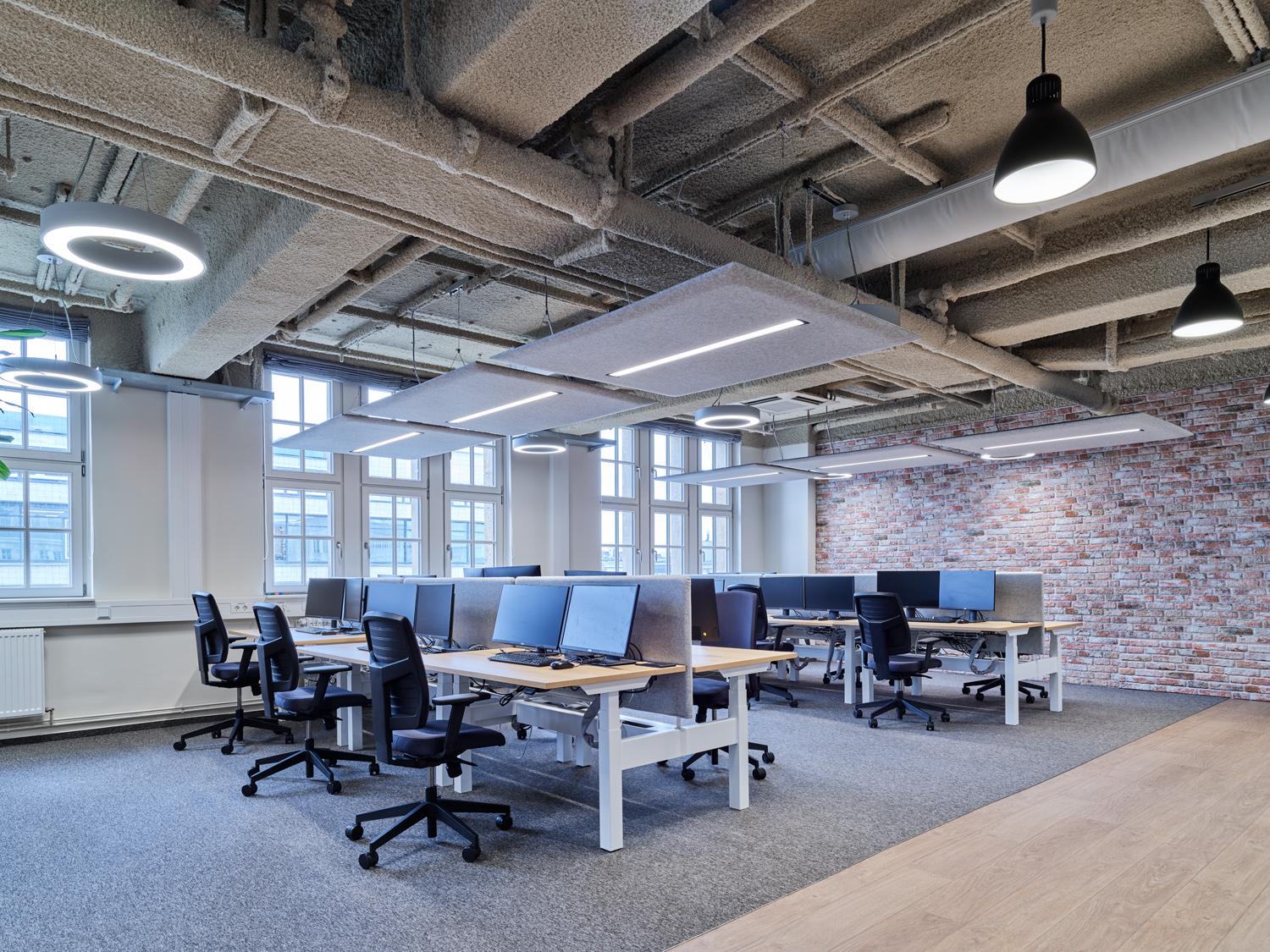 Open office with modern desks, acoustic ceiling panels and large windows with natural light