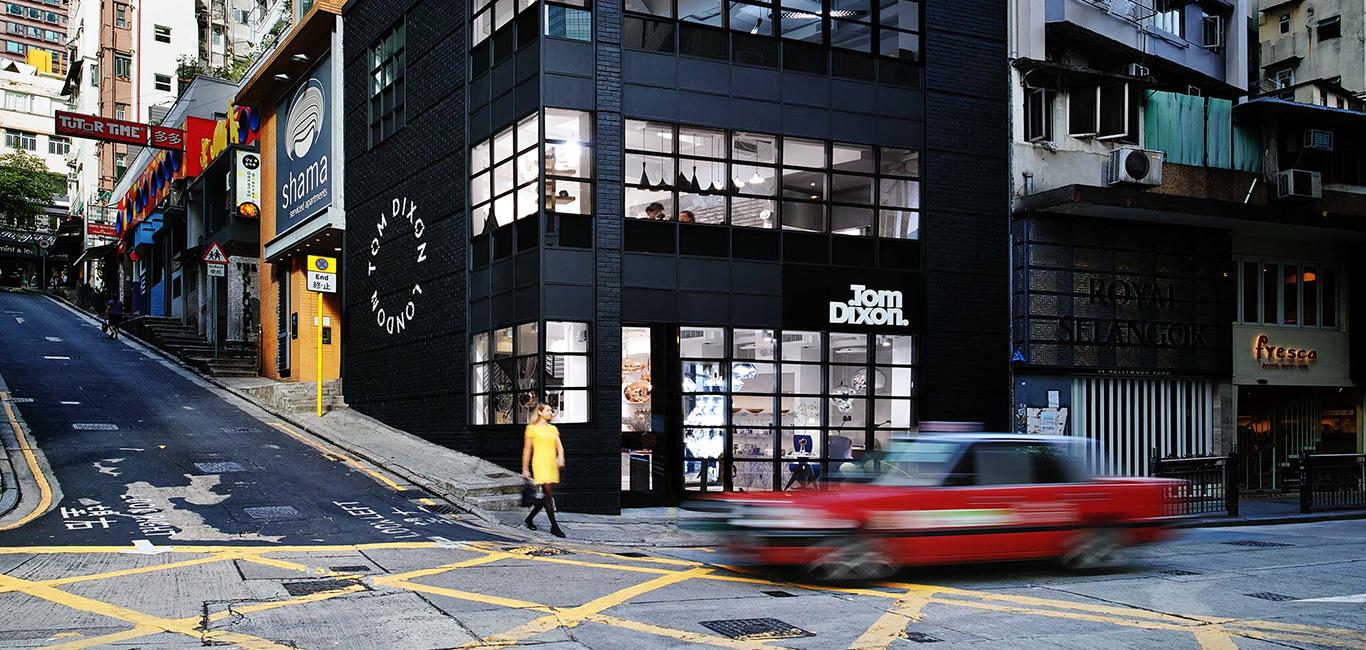 Red car driving past modern black building on busy street in Hong Kong